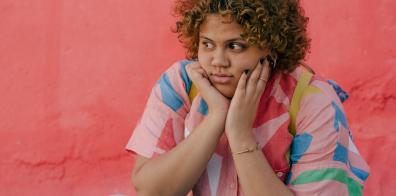 Woman in colourful T-shirt with head in hands looking fed up.
